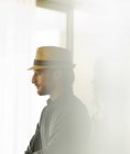 Jeune homme attrayant en chapeau de paille regardant par la fenêtre — Photo de stock