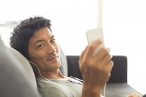Joven atractivo Hombre escuchando los auriculares en el sofá - foto de stock