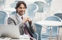 Ritratto di uomo d'affari sorridente con laptop ed espresso al caffè sul marciapiede — Foto stock