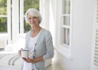 Mujer mayor sosteniendo una taza de café en la sala de sol - foto de stock