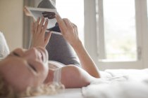 Сміється жінка лежить в ліжку за допомогою цифрового планшета — стокове фото
