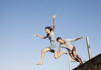 Happy exuberant couple jumping off dock — Stock Photo
