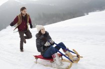 Счастливая пара катается на санках по снежному полю — стоковое фото