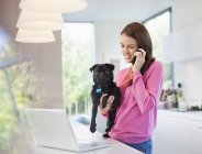 Woman on cell phone holding dog at modern home — Stock Photo
