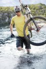 Спортивний чоловік, що перевозить гірський велосипед у річці — стокове фото