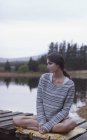 Donna pensierosa seduta sul molo al lago — Foto stock