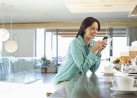 Donna che utilizza il telefono cellulare in cucina — Foto stock