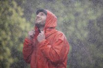Homem sorridente com capa de chuva olhando para a chuva — Fotografia de Stock