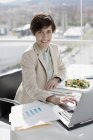 Portrait of smiling businesswoman eating lunch and working at desk — Stock Photo