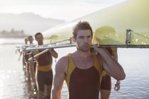 Rowing team carrying scull out of lake — Stock Photo