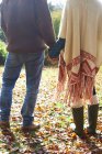 Coppia che si tiene per mano in foglie di autunno — Foto stock
