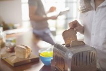 Женщина кладет хлеб в тостер — стоковое фото