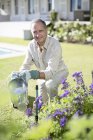 Старший кавказский мужчина поливает растения в саду — стоковое фото