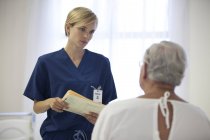 Enfermera y paciente mayor hablando en la habitación del hospital - foto de stock