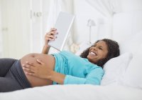 Femme enceinte utilisant un ordinateur tablette sur le lit — Photo de stock