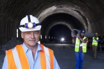 Empresário em pé no túnel contra trabalhadores com tubo — Fotografia de Stock
