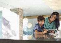 Mother and son using tablet computer in kitchen — Stock Photo