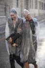 Businesswomen in ponchos walking in rainy street — Stock Photo