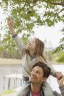 Daughter on father?s shoulders reaching for branch — Stock Photo
