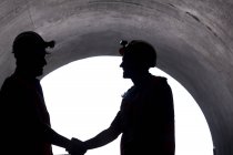 Silhueta de trabalhadores apertando as mãos em túnel — Fotografia de Stock