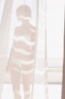 Frau in BH und Unterwäsche hinter sonnigem Vorhang — Stockfoto