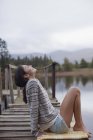 Улыбающаяся женщина, сидящая на причале у озера со спиной — стоковое фото