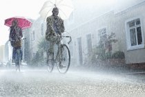 Couple with umbrellas riding bicycles in rain — Stock Photo