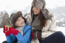 Счастливая мать и сын пьют горячий шоколад на снежном поле — стоковое фото