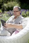 Старший использует цифровой планшет в кресле — стоковое фото