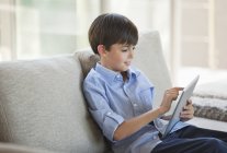 Хлопчик використовує планшетний комп'ютер на дивані — стокове фото