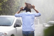 Vista trasera del hombre que cubre la cabeza con periódico en la calle lluviosa - foto de stock