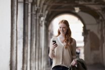 Smiling woman checking cell phone in corridor — Stock Photo