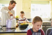 Father and son juicing vegetables in kitchen — Stock Photo