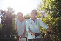 Senior couple walking bicycles in park — Stock Photo