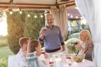 Senior homme griller la famille avec du vin rouge à la table de patio — Photo de stock