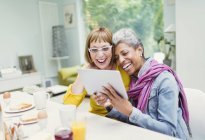 Lachende reife Frauen teilen digitales Tablet am Frühstückstisch — Stockfoto