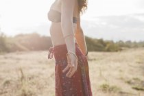 Boho woman in bikini top and skirt with arms outstretched in sunny rural field — Stock Photo