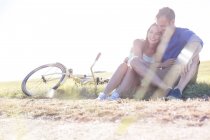 Casal jovem afetuoso abraçando perto de bicicleta na grama rural — Fotografia de Stock