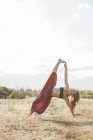 Boho woman in extended side plank yoga pose in sunny rural field — Stock Photo