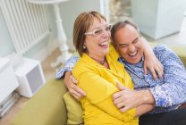 Зрелая пара смеется и обнимается на диване — стоковое фото