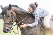 Lächelnde Frau reitet schief und streichelt Pferd — Stockfoto