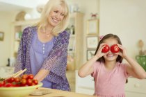 Portrait petite-fille ludique couvrant les yeux avec des tomates dans la cuisine — Photo de stock