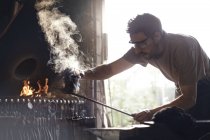 Blacksmith shaping steaming wrought iron in forge — Stock Photo