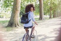 Portrait smiling woman with afro riding bicycle in park — Stock Photo