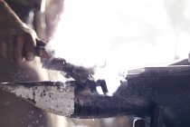 Крупный план кузнеца, чистящего железный инструмент над наковальней в кузнице — стоковое фото