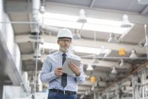 Engineer with hard-hat and digital tablet walking in factory — Stock Photo