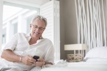 Uomo più anziano utilizzando il telefono cellulare sul letto — Foto stock