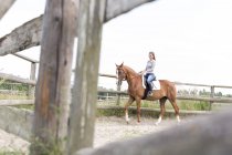 Woman horseback riding in fenced rural pasture — Stock Photo