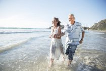 Older couple playing in waves on beach — Stock Photo