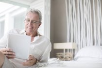 Uomo più anziano utilizzando tablet digitale sul letto — Foto stock